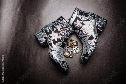 Fototapeta Naklejka Na Ścianę i Meble -  black thick-heeled ankle boots decorated with flowers embroidered with silver sequins and brooches on a gray paper background