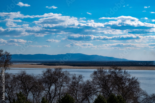 View of the Amur river against the blue sky with white beautiful clouds. Bright spring sun. Russia, Khabarovsk.