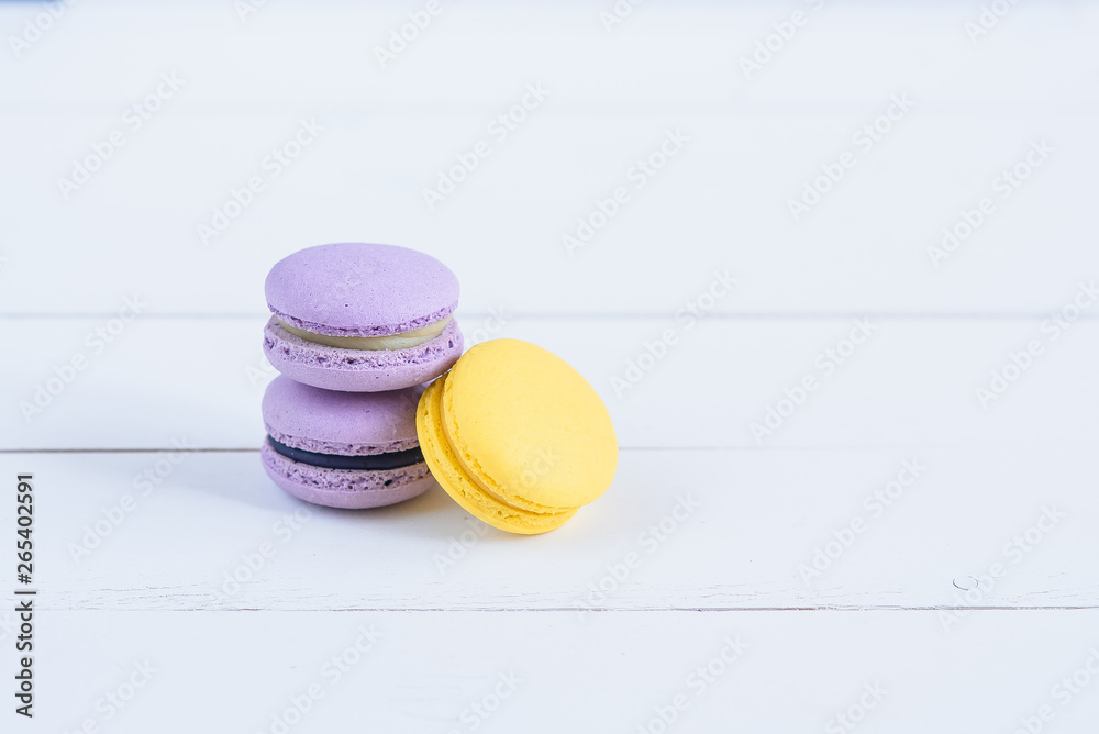 Obraz premium Delicious violet and yellow macarons on white wooden background.