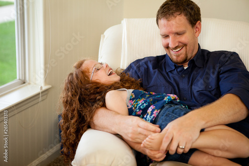 Father Tickling Daughter on Chair at Home