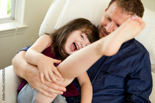 Father Tickling Daughter on Chair at Home