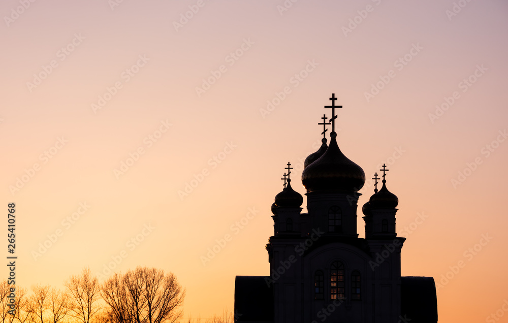 A cropped silhouette of a Christian church and trees against background of clear sunset sky. Peaceful scene, warm tones, high contrast.