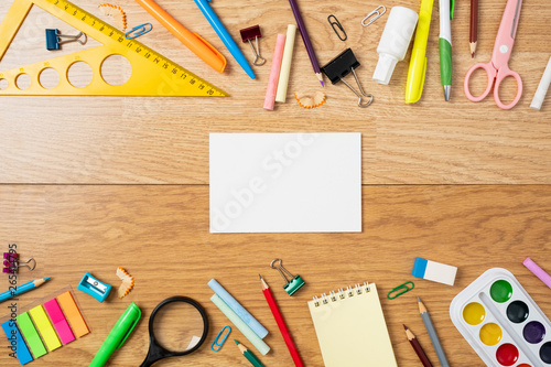 Frame made of stationery and blank paper card in the center, school supplies on wooden table. Education, studying and back to school concept. Child desk top view, copy space, flat lay composition.