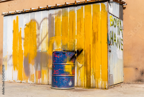 Blue metal drum in front of a shed painted in white and yellow. Text on the door: Dye house photo