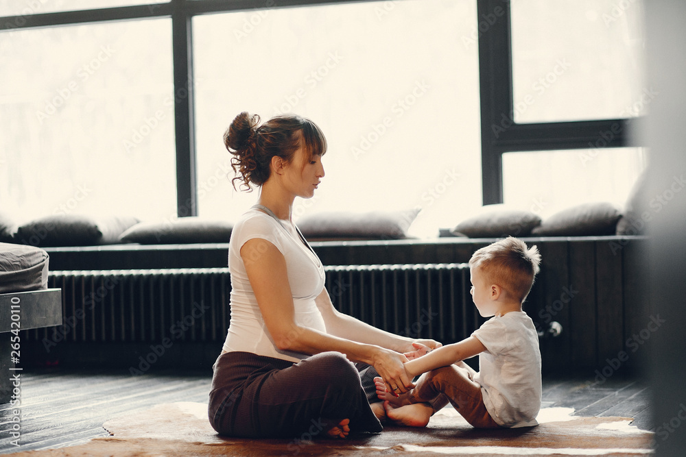 Pregnant woman at home. Mother with son doing yoga. Family in a room with large windows