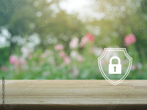 Padlock with shield flat icon on wooden table over blur pink flower and tree in garden, Business security insurance concept