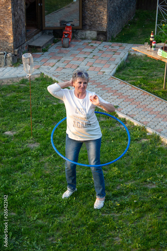 Elderly woman trains in nature with a hoop.