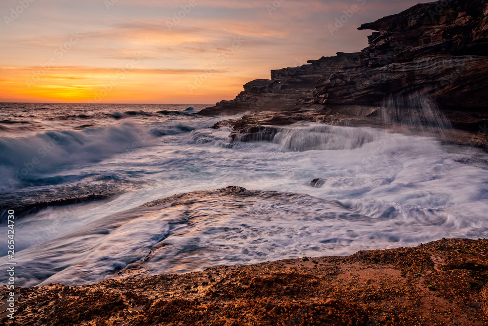 Sunrise and ocean cascades along coastal rocks and headland