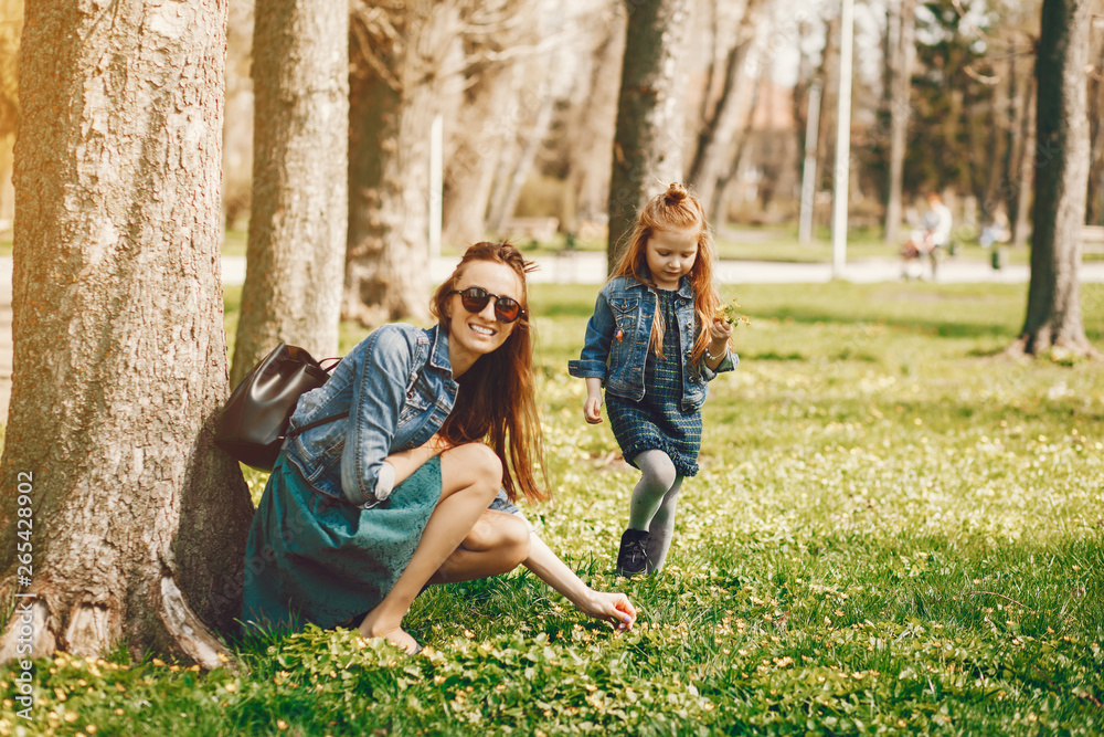 Fototapeta premium young and stylish mother with long hair and a jeans jacket playing with her little cute daughter in the summer park