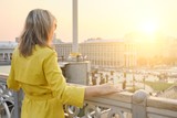 Rear view of woman looking at panorama of evening city. Adult female in yellow raincoat outdoor, copy space, golden hour