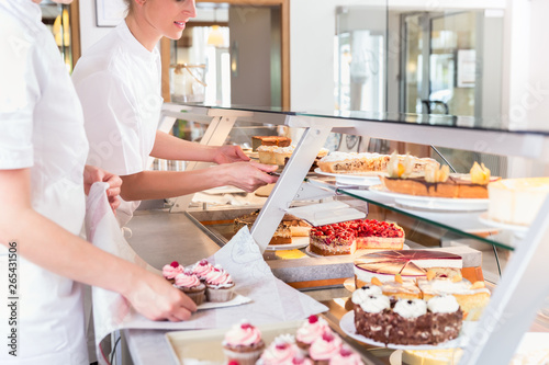 Women in pastry shop filling up sales display with pies