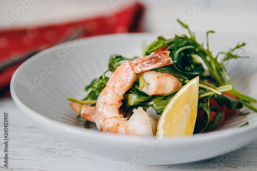 Closeup Salad with shrimps, arugula, lemon, tomatoes in deep bowl. Table setting is light