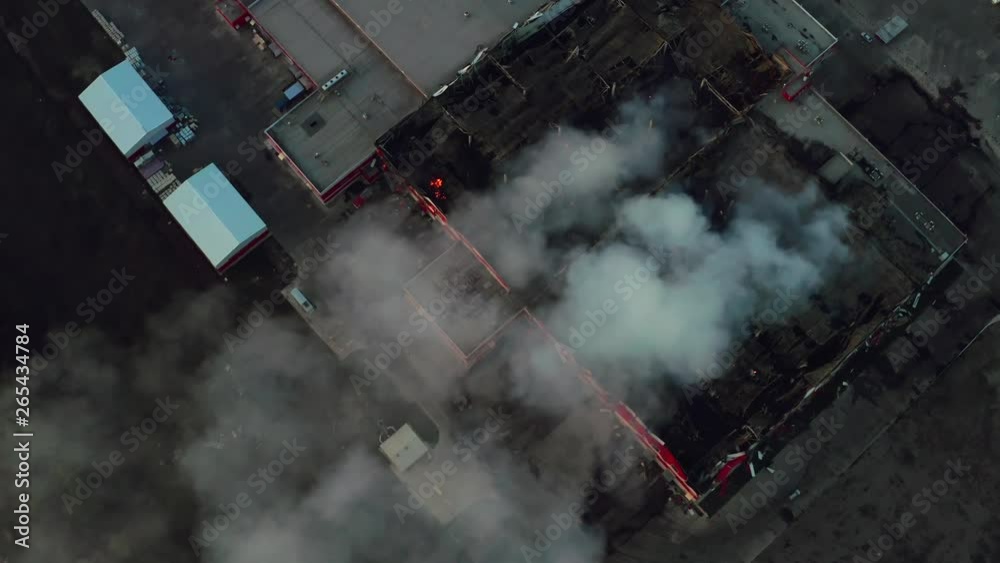 Aerial view of smoke clouds from burnt warehouse building with burned roof, fire disaster accident in cargo logistics storehouse, drone footage