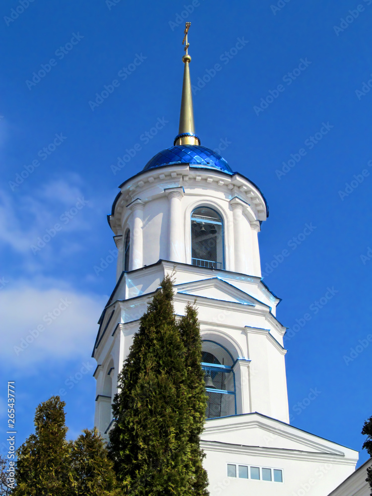 Sumy, Ukraine - April 1, 2019: Bell tower of the Orthodox Elias temple in Sumy, close-up, vertical. Church tower in a classicism architectural style with white walls, a blue dome and a golden cross