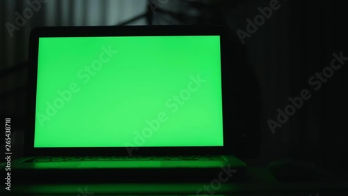 Laptop with green screen. Dark office.  Perfect to put your own image or video.Green screen of technology being used. Chroma Key laptop
