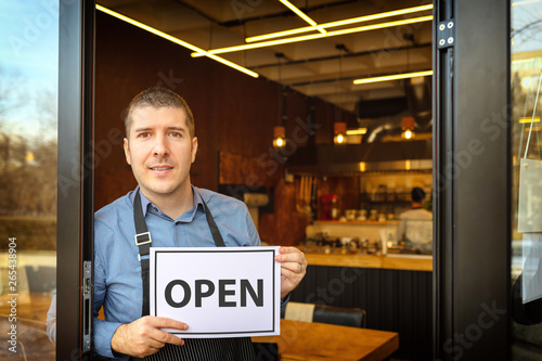 Billede på lærred Portrait of happy business owner holding open sign at entrance of new small fami