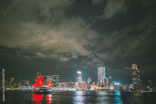 Panorama of Hong Kong City skyline with tourist sailboat at night.