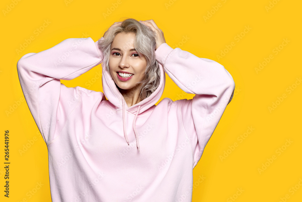 Portrait of adorable blonde young female wearing blank pink sweatshirt and posing on yellow background. Happiness and lifestyle concept. Copy space in right side Portrait of adorable blonde young female wearing blank pink sweatshirt and posing on yellow background. Happiness and lifestyle concept. Copy space in right side
