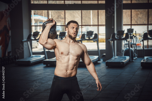 athletic young man with beard doing lifting weight at the gym opposite the camera. exercise on the shoulders with weight dumbbells. Guide how to do lifts for shoulders
