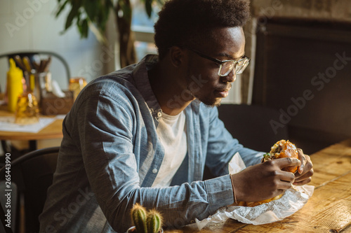 african american man enjoying the taste of hamburger.handsome and young afro man in a stylish shirt and glasses holding a burger on a white background.love of junk food diet