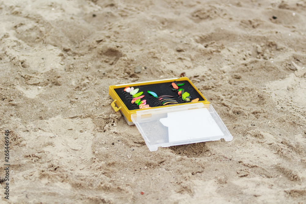 Obraz premium Fishing. Colorful fishing lures in a box. A fishing box lying on the sand