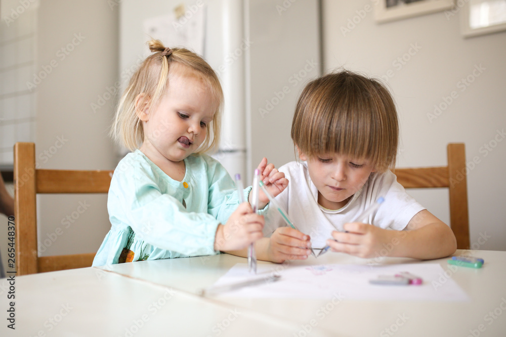 Children siblings paint at table in white kitchen Children siblings paint at table in white kitchen