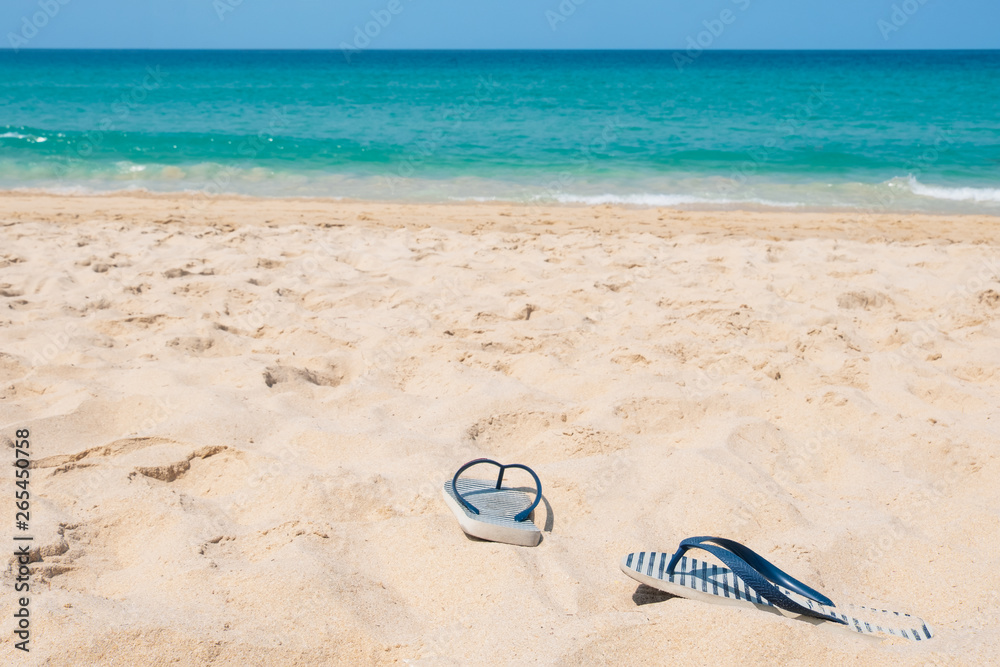 Summer vacation concept. Slippers on tropical beach. Sandy beach with sea and blue sky background. Summer, holiday -Image Summer vacation concept. Slippers on tropical beach. Sandy beach with sea and blue sky background. Summer, holiday -Image