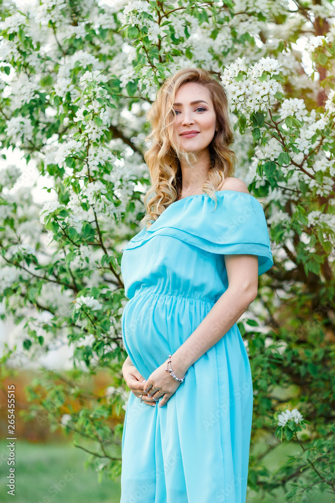 Beautiful pregnant woman in blue dress is standing near the cherry blossom. Pregnant young happy women in blossom white garden.Pregnant pretty woman in spring blossom garden. Beautiful pregnant woman in blue dress is standing near the cherry blossom. Pregnant young happy women in blossom white garden.Pregnant pretty woman in spring blossom garden.