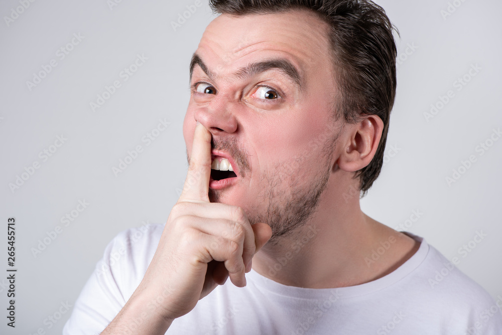 Handsome guy with bristles in a white t-shirt picks his finger in his nose Handsome guy with bristles in a white t-shirt picks his finger in his nose