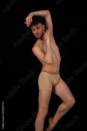 The gymnastic pose of the Caucasian man dances in the studio with plastic hand and leg positions. The attractive young man shows modern dance poses, on a black background.