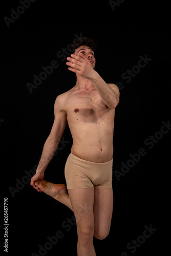 The gymnastic pose of the Caucasian man dances in the studio with plastic hand and leg positions. The attractive young man shows modern dance poses, on a black background.