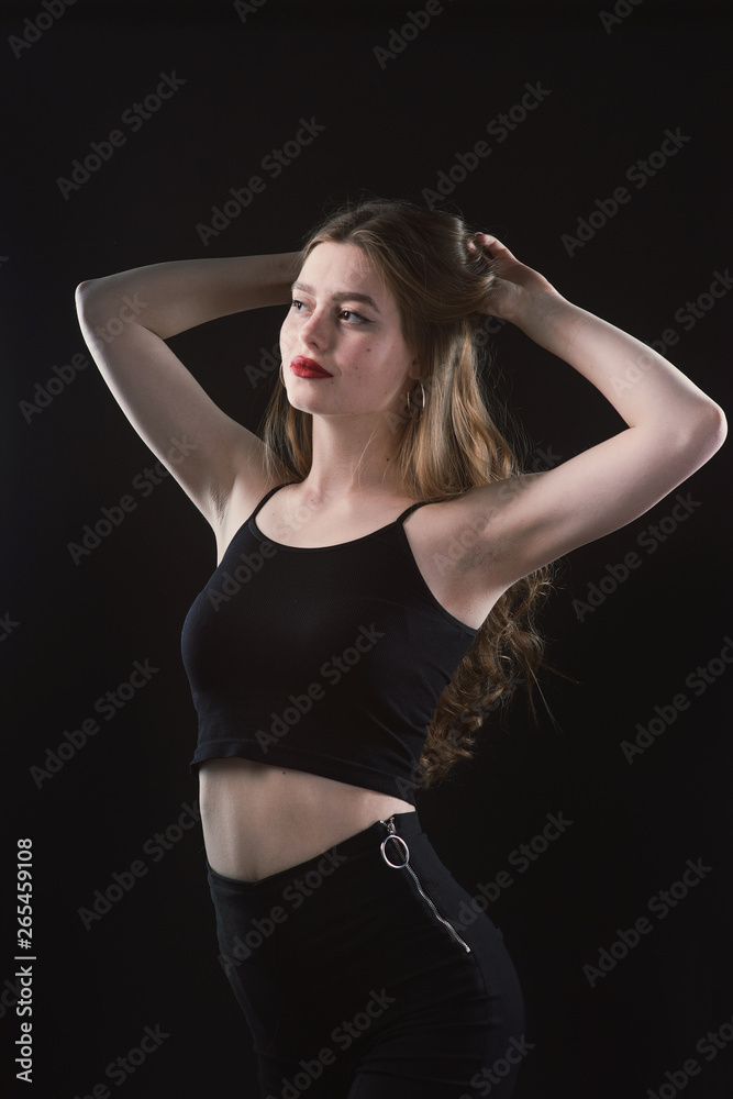 Young beautiful, slender, passionate brown-haired woman with bright red lips and long hair in a black top and denim shorts on a dark background Young beautiful, slender, passionate brown-haired woman with bright red lips and long hair in a black top and denim shorts on a dark background