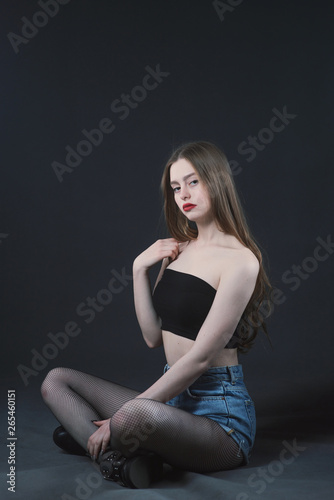 Young beautiful, slender, passionate brown-haired woman with bright red lips and long hair in a black top and denim shorts on a dark background © Антон Фрунзе
