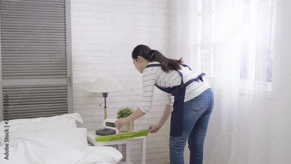 Happy asian female chambermaid making bed in hotel room. young mom with further duster wearing apron cleaning up bedroom of children in day time. chinese housewife daily routine job work at home. Happy asian female chambermaid making bed in hotel room. young mom with further duster wearing apron cleaning up bedroom of children in day time. chinese housewife daily routine job work at home.