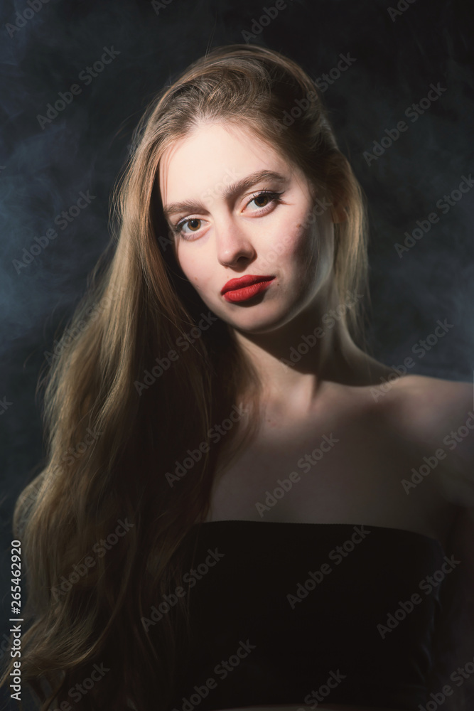 Young beautiful, slender, passionate brown-haired woman with bright red lips and long hair in a black top and denim shorts on a dark background Young beautiful, slender, passionate brown-haired woman with bright red lips and long hair in a black top and denim shorts on a dark background