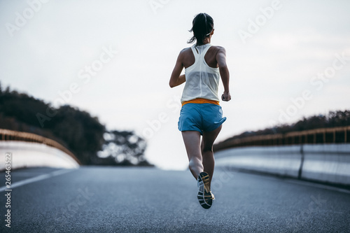 Young fitness woman running on city road