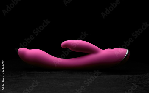 Pink vibrator on black skin. Dark background.