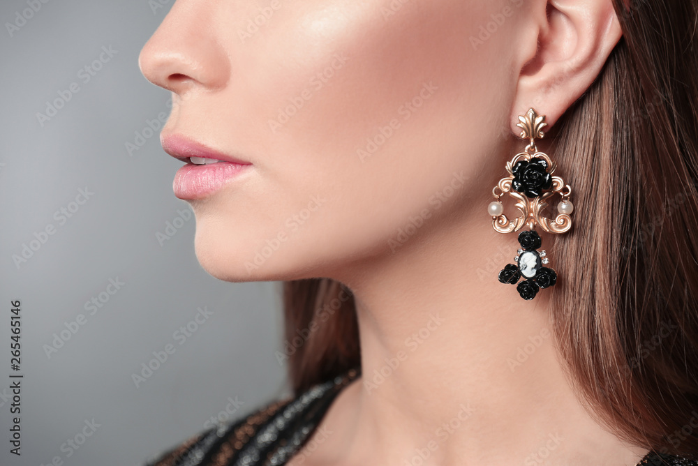 Beautiful woman with stylish jewelry on grey background, closeup