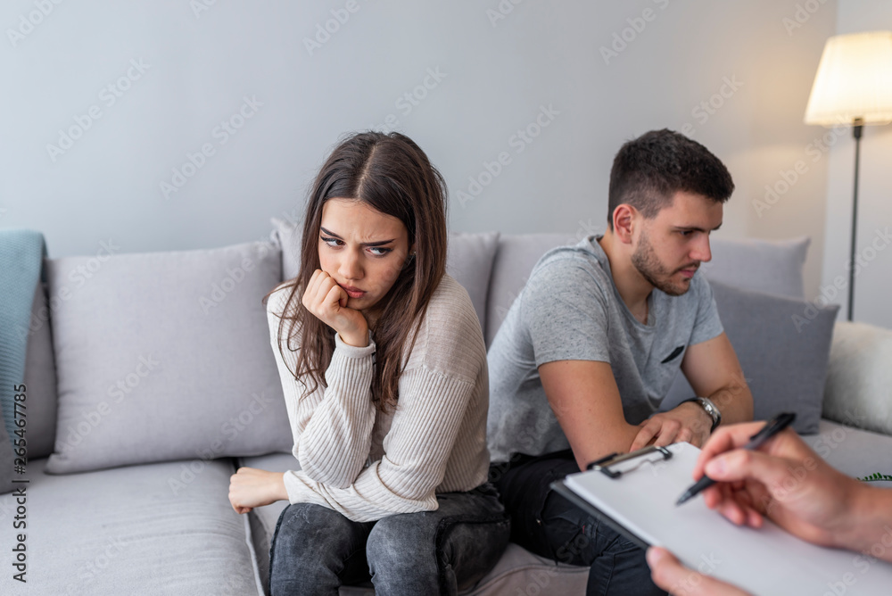 Angry husband and sad wife talking with a marriage counselor before breaking up sitting on a sofa at home. Young couple having marriage counselling Angry husband and sad wife talking with a marriage counselor before breaking up sitting on a sofa at home. Young couple having marriage counselling
