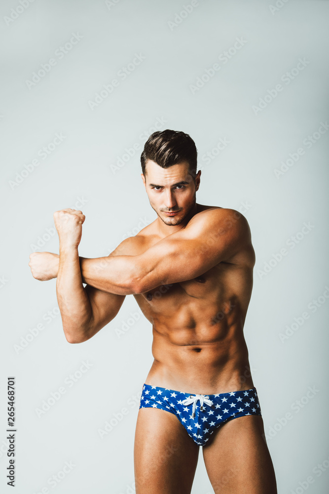 Portrait of handsome young man with stylish haircut in Amrican stars swimwear posing over gray background. Perfect hair & skin. Close up. Studio shot