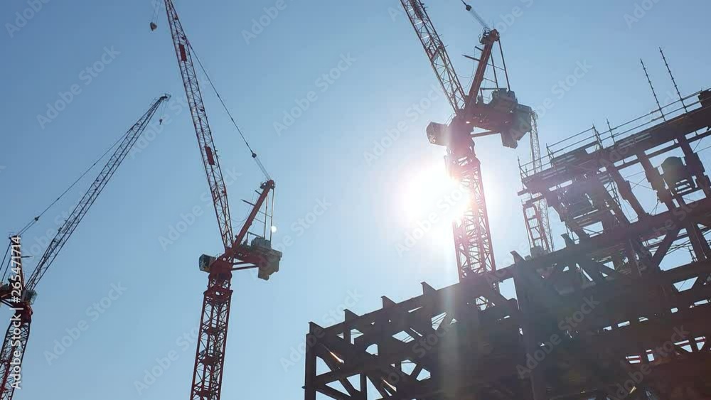 Construction cranes on the background of the blue sky and the bright sun, which is hidden behind the construction crane