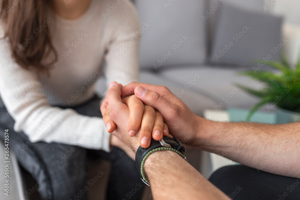 Fototapeta premium Hands of man supporting his best friend. Concept of support - man and woman holding hands in the light room. Supporting a friend in need. Male hands holding female, caring loving understanding man