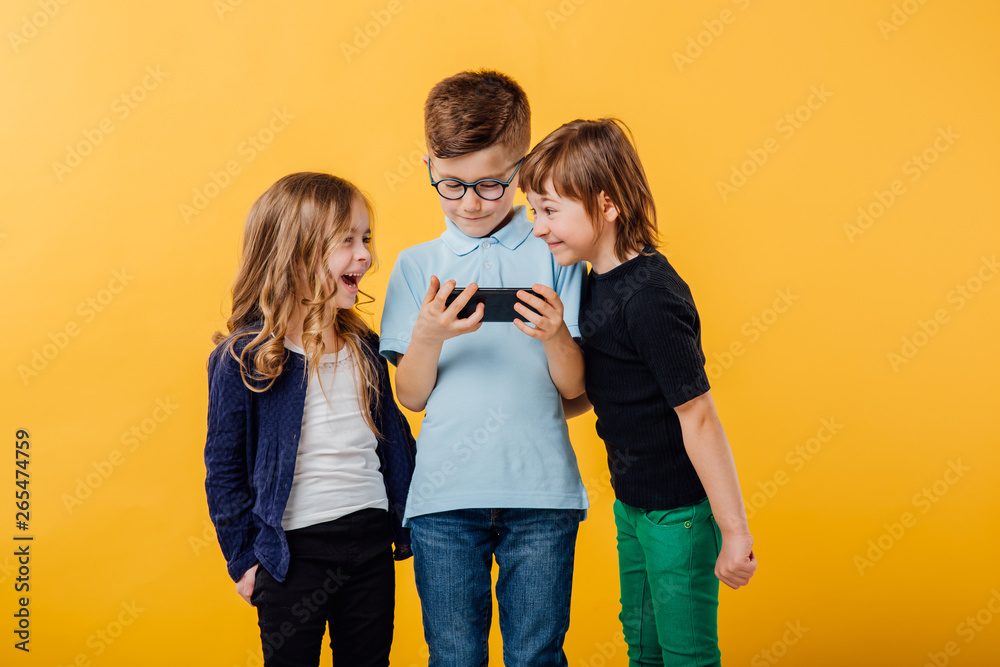 Φωτογραφία three, little boy and two little girls are happy, look at the phone, are cheerfu