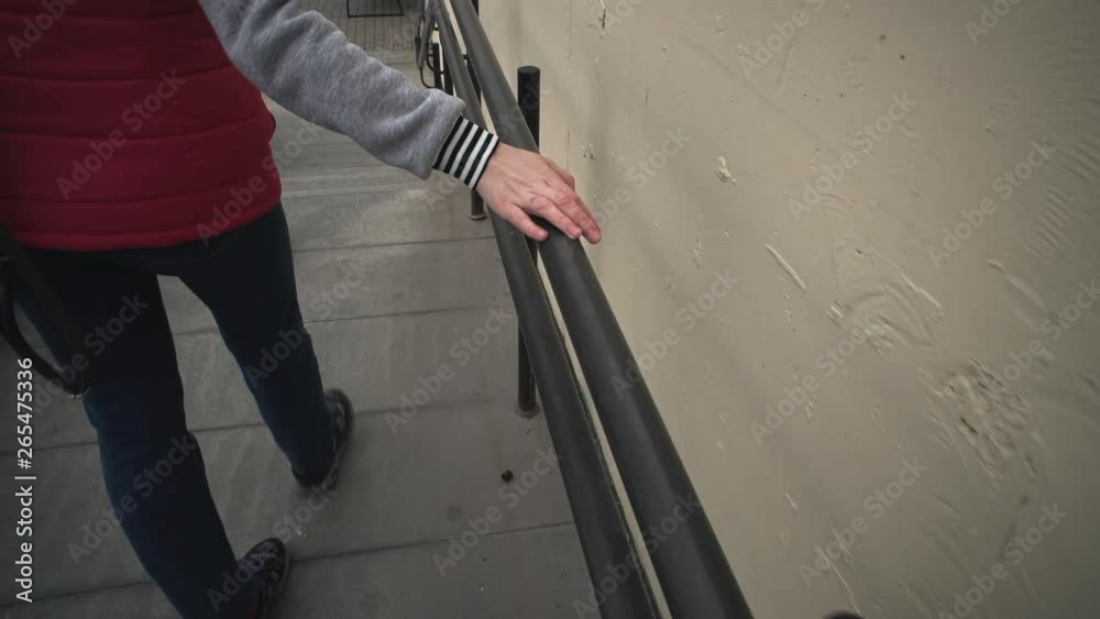 A young woman in a red jacket walks and touches a metal black railing ...