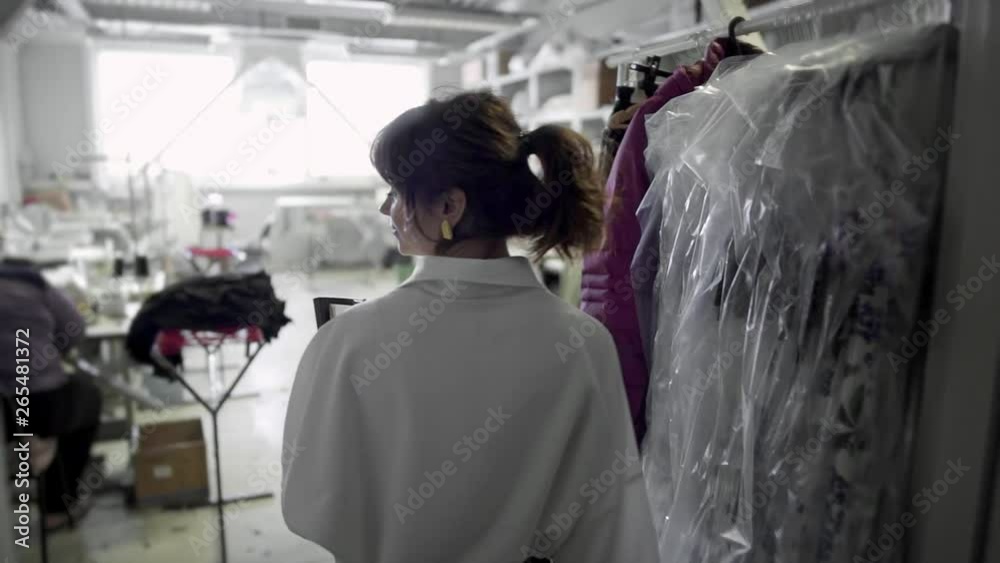 Slow motion of designer coming in seamstress studio with woman working sewing. Female fashion designer watching for the work of group of seamstresses in sewing studio Slow motion of designer coming in seamstress studio with woman working sewing. Female fashion designer watching for the work of group of seamstresses in sewing studio