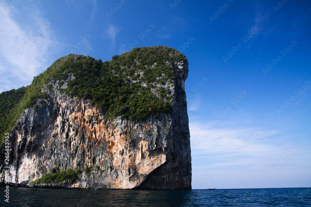 Fototapeta premium Isolated steep rough cliff in the ocean rising into blue sky of tropical island Ko Phi Phi, Thailand