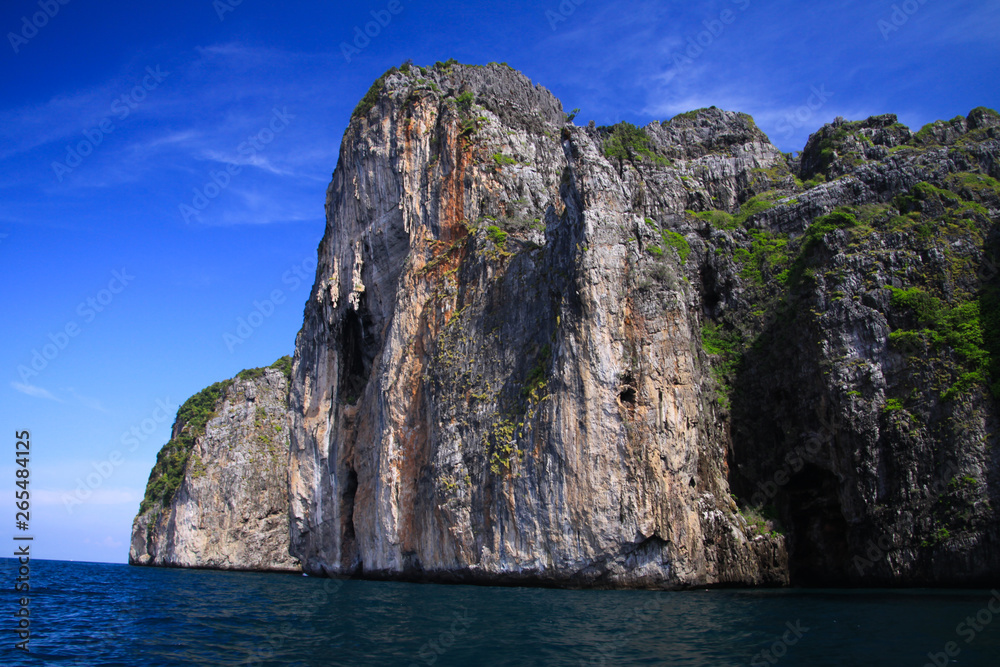 Boat trip along the coast line of tropical island Ko Phi Phi along impressive rock formations under blue sky
