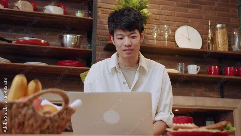 Young man sit and use laptop work in the morning at home in kitchen portrait male morning asia asian casual chinese guy, social media internet notebook pc portrait close up slow motion Young man sit and use laptop work in the morning at home in kitchen portrait male morning asia asian casual chinese guy, social media internet notebook pc portrait close up slow motion