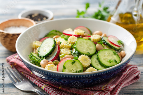 Healthy vegetable salad with cucumber, radish, beans, mini corn and herbs on rustic wooden background. Selective focus.