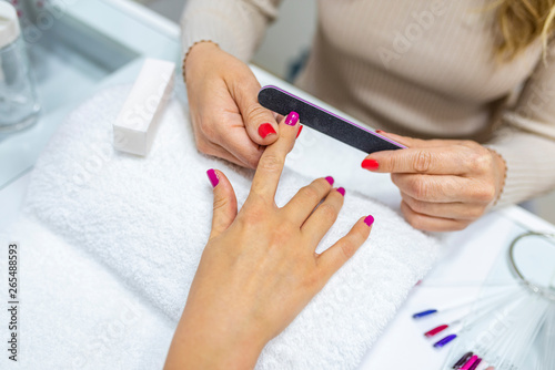 Closeup shot of a woman in a nail salon receiving a manicure by a beautician at nail salon. Woman using a buffer for file nail. Shallow depth of field with focus on nailfile.